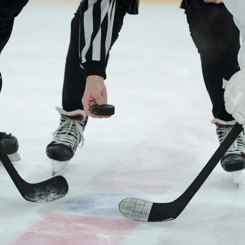 Hockey faceoff with referee dropping puck.